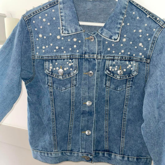 A denim jacket with pearl detail on the collar and chest area, displayed on a white hanger.