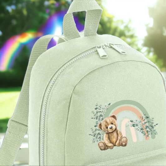 Mint green backpack featuring a teddy bear design with a rainbow motif, suitable for children.