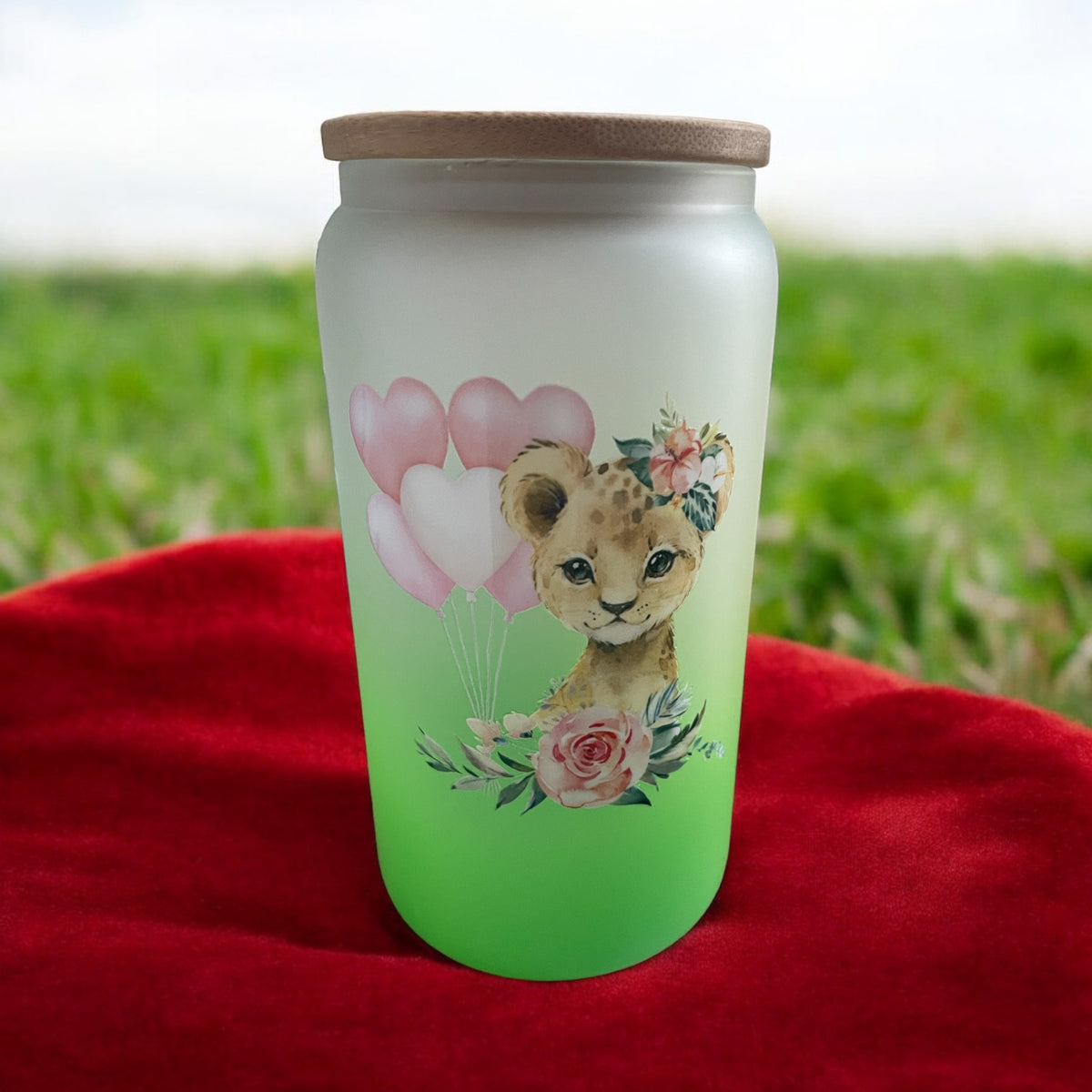 A 16oz green ombre glass with a bamboo lid and a glass straw, featuring a cartoon lioness with balloons and flowers design.