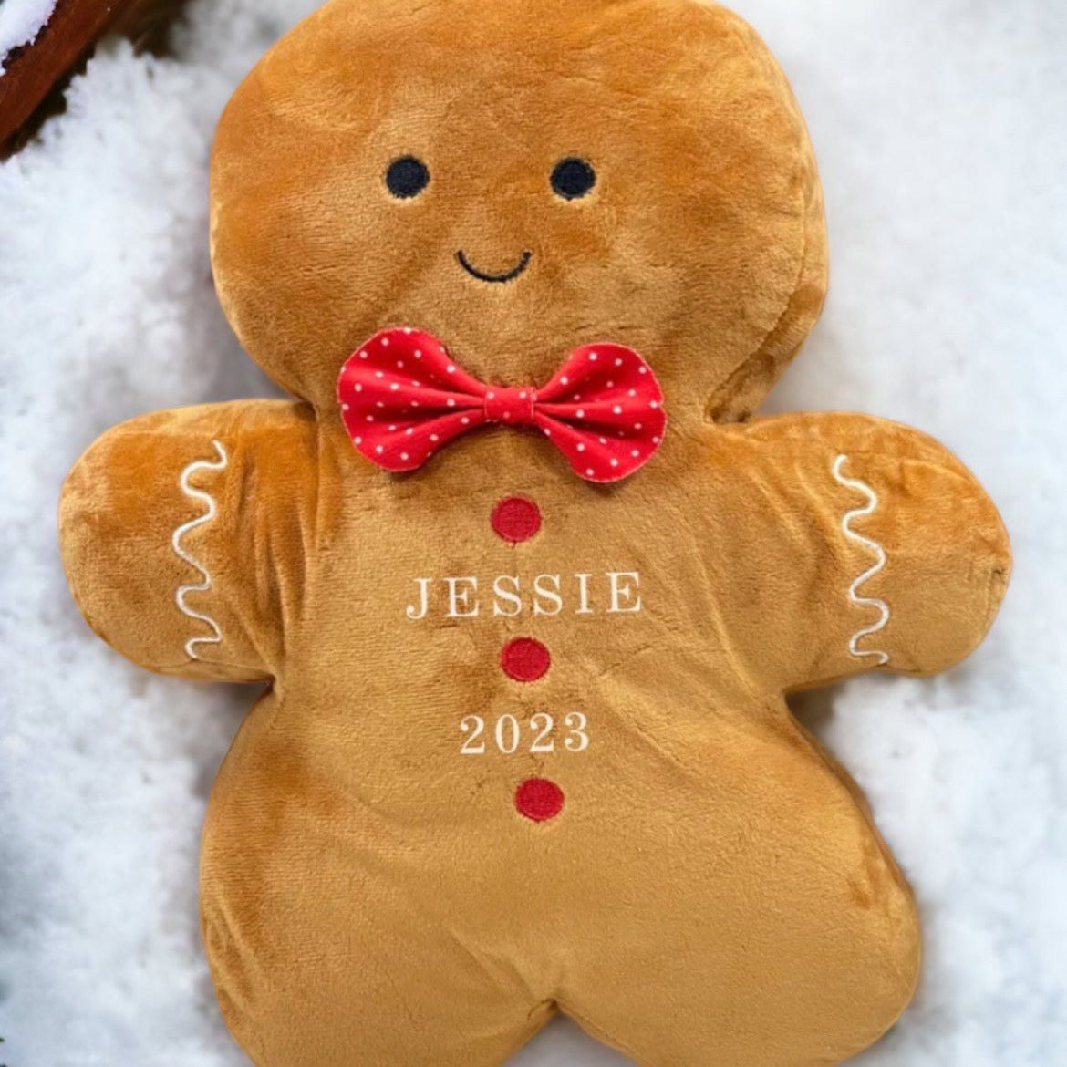 A plush toy resembling a gingerbread man with the name 'Jessie' and the year '2023' printed on it, placed on a snowy surface.