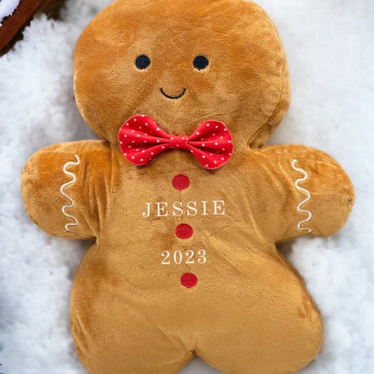 A plush toy resembling a gingerbread man with the name 'Jessie' and the year '2023' printed on it, placed on a snowy surface.
