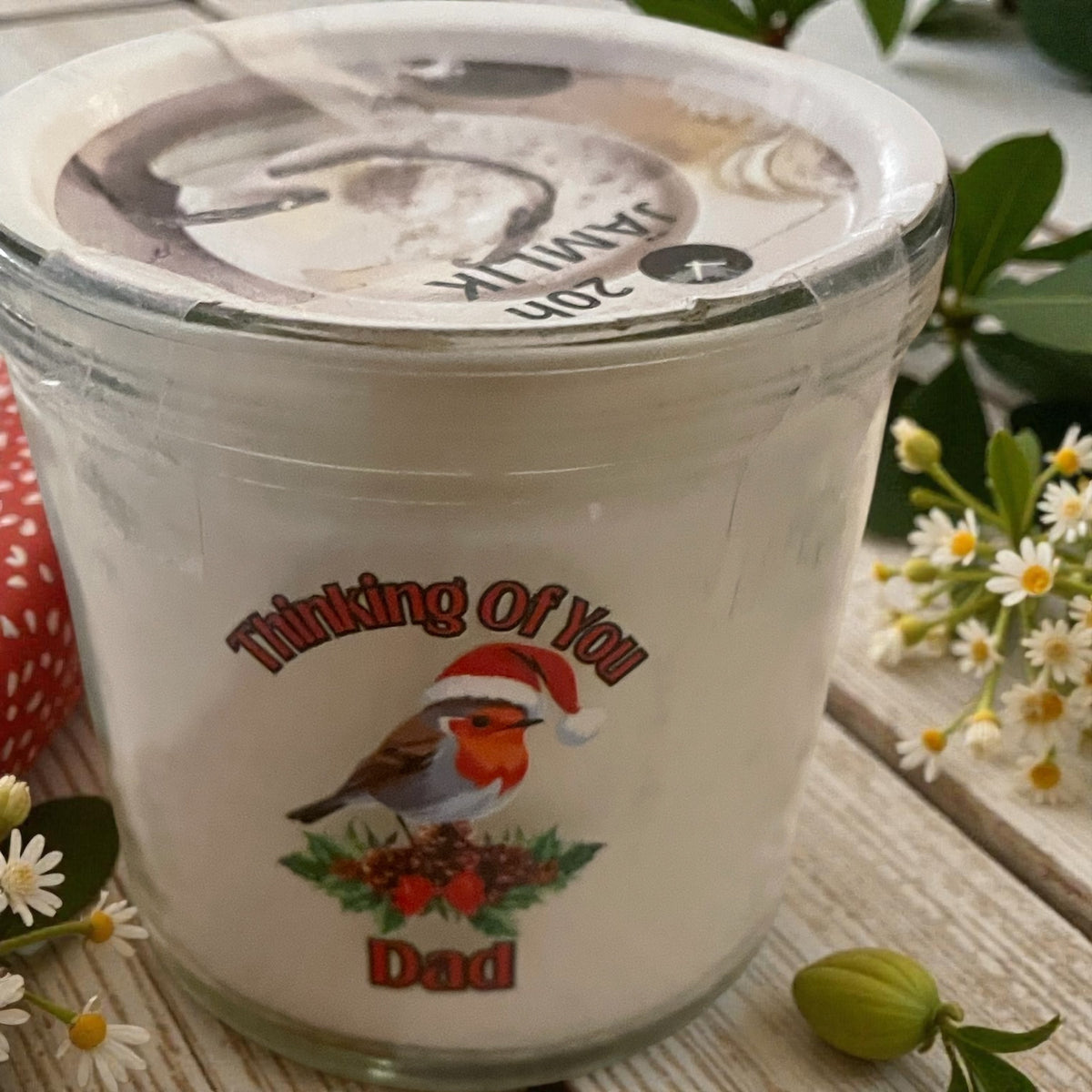 Glass container with a lid featuring a bird illustration and text, surrounded by flowers and leaves.