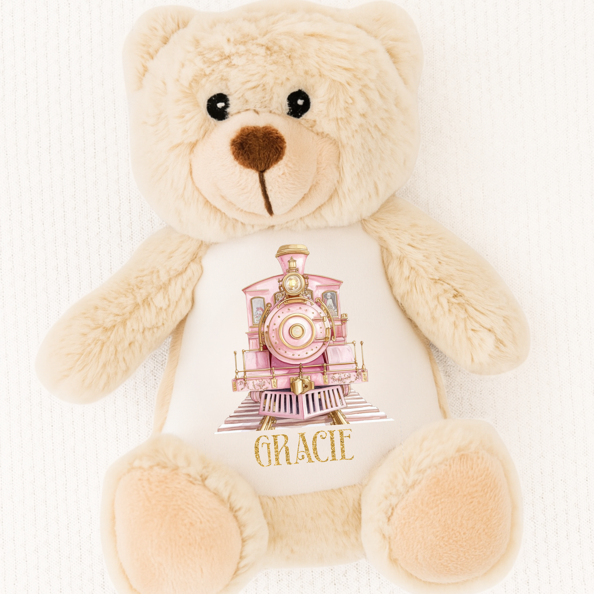 Beige teddy bear with a white shirt featuring a pink train design and the name 'Gracie' on a white background.