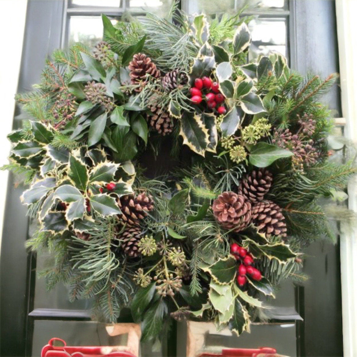 Christmas wreath with greenery, pine cones, and berries on a door.