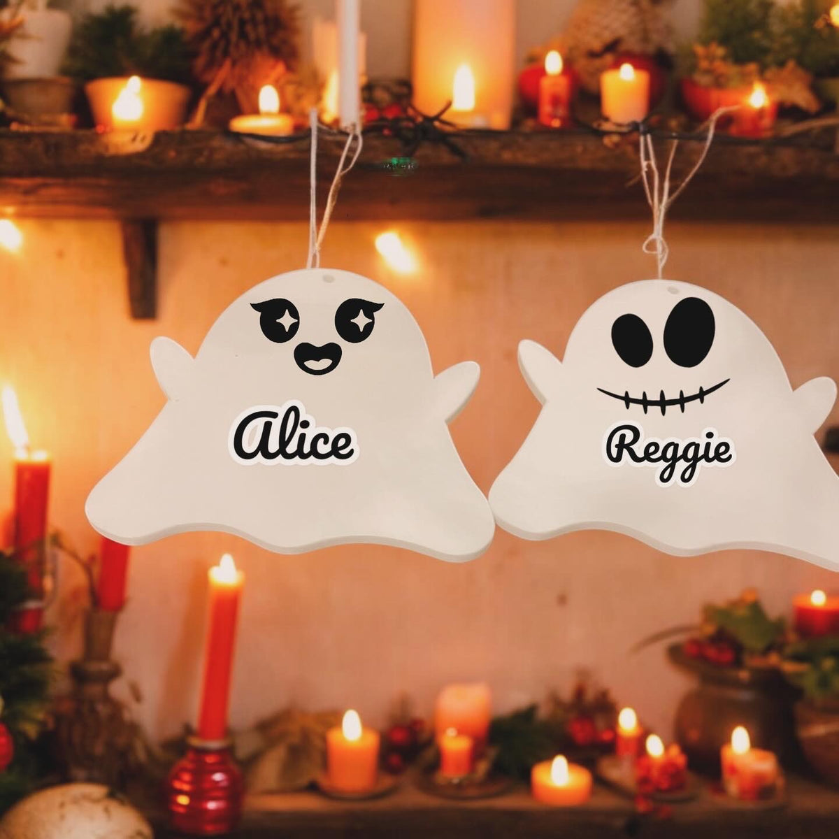 Two personalized acrylic ghosts hanging by ribbons, with one displaying a smiling face and the other a frowning face, both with the names 'Alice' and 'Reggie' written on them respectively.