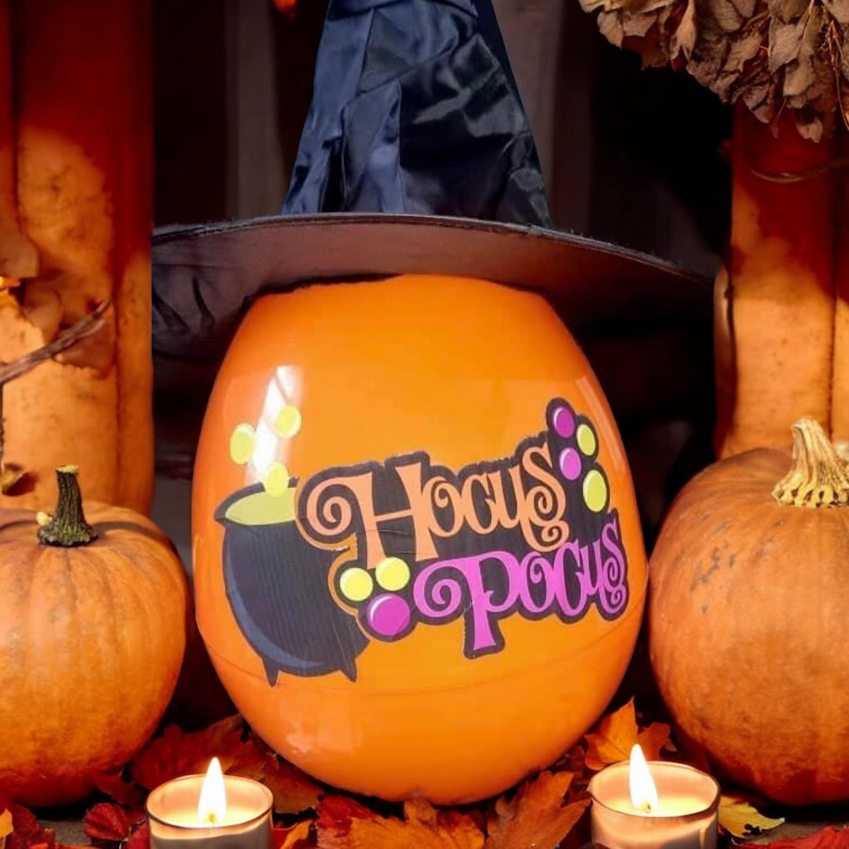 A personalized orange stuffable egg with 'BOO' text design, decorated with pumpkin and witch illustrations, displayed on a table with pumpkins and a witch's hat in the background.