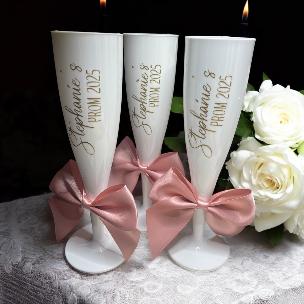 Three white champagne flutes with pink bows and 'Stephanie's Prom 2025' text, surrounded by white roses on a dark background.
