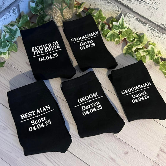 Black socks with personalized text on a wooden surface with greenery