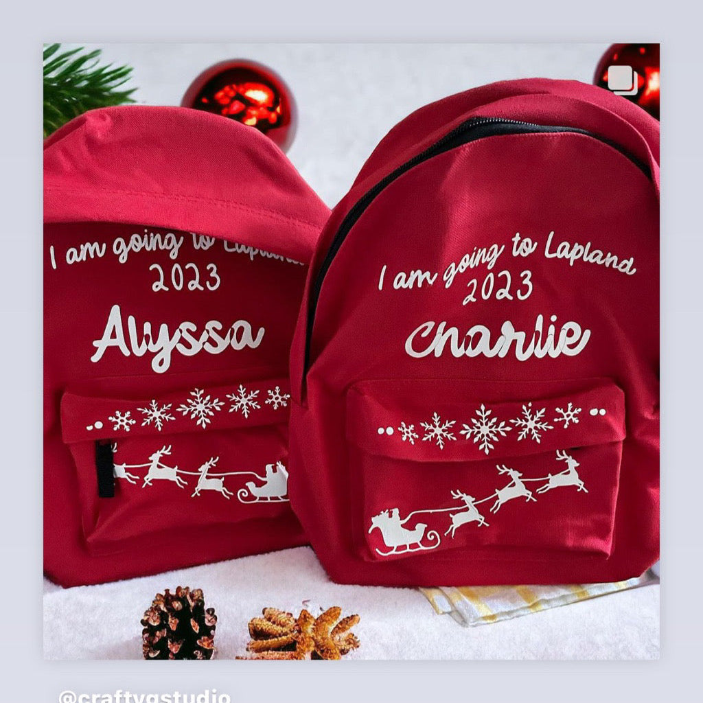 Two red backpacks, one with 'Alyssa' and the other with 'Charlie' text, both with a Christmas-themed design featuring a reindeer.