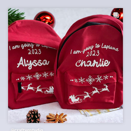 Two red backpacks, one with 'Alyssa' and the other with 'Charlie' text, both with a Christmas-themed design featuring a reindeer.