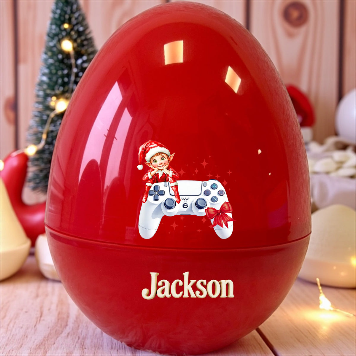 Red egg-shaped container with a design of a video game controller and elf, labeled 'Jackson', on a wooden surface with Christmas decorations.