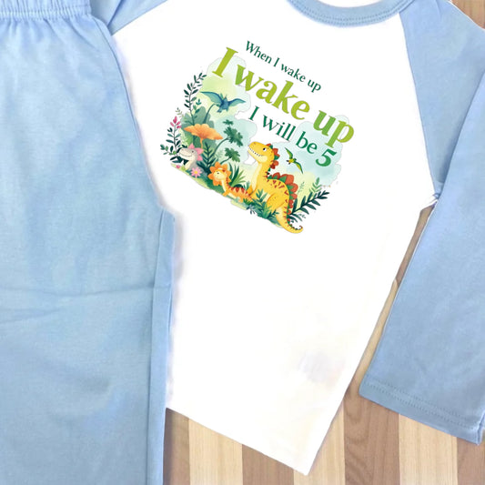 Children's outfit with a dinosaur-themed shirt and light blue pants on a wooden surface.