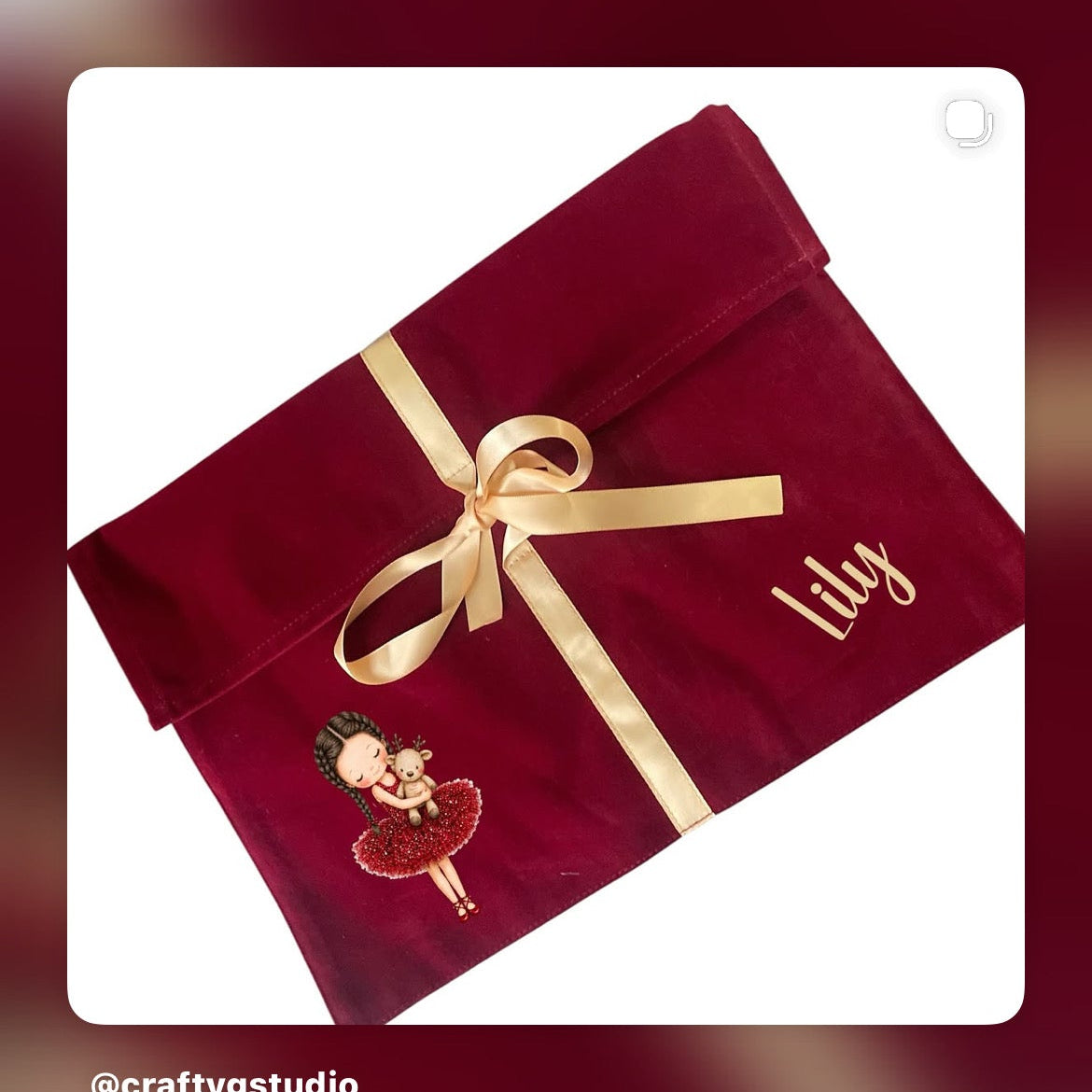 A personalized burgundy velvet gift pouch with a gold ribbon and bow, featuring a custom embroidered ballerina and the name 'Lily' in gold script. The pouch is displayed on a white card with a blurred burgundy background.