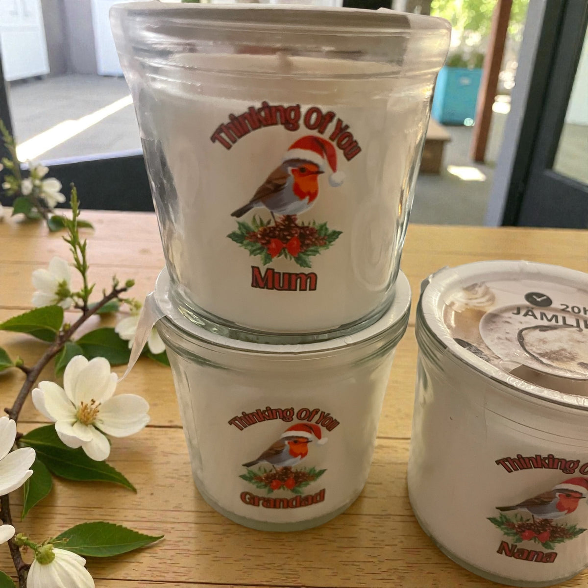 Stack of ceramic containers with 'Thinking Of You' and 'Mum' text on a wooden surface with flowers.