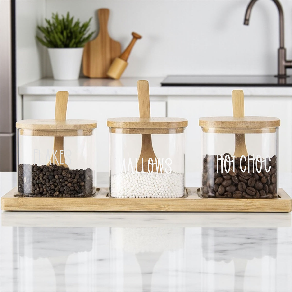 Three glass jars with wooden lids on a kitchen counter, labeled 'KE', 'ALLOWS', and 'HOT CHOC'.