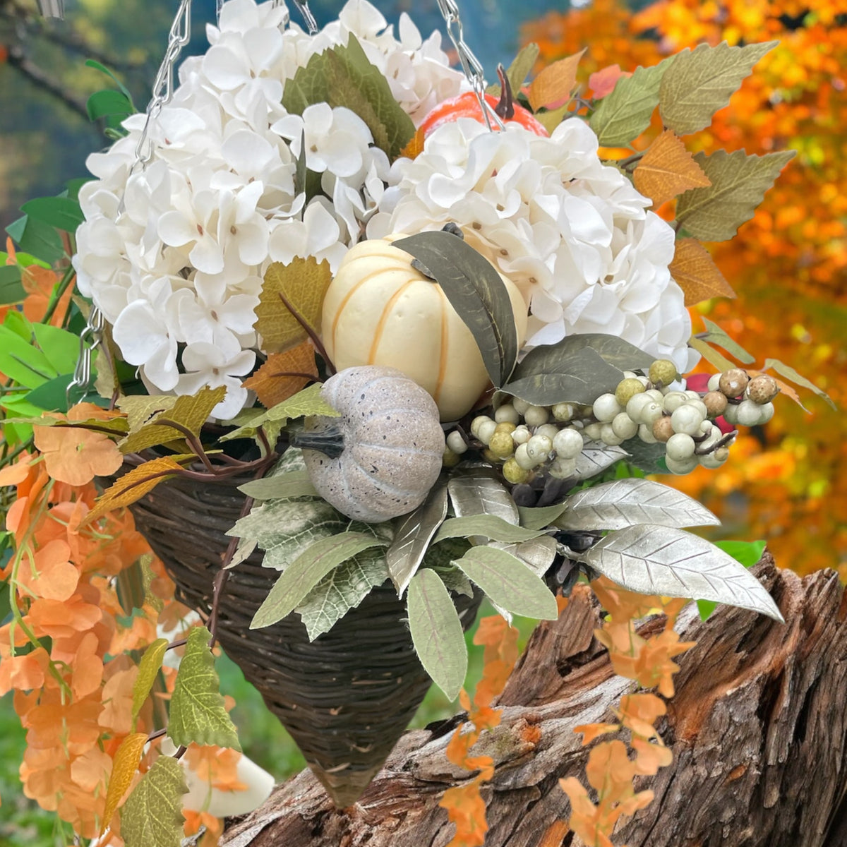 A hanging basket decorated with white hydrangeas, burnt orange leaves, pumpkins, berries, and maple leaves, with a focus on autumn colors.