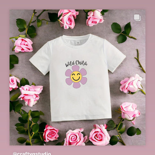 A white t-shirt with a floral design and the text 'Wild Child' on it, presented on a background with pink flowers and leaves.